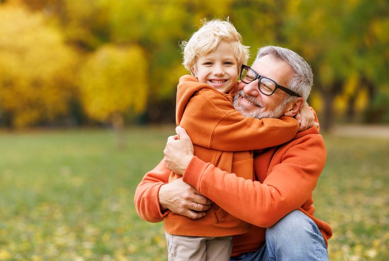 Grandfather hugging grandson outdoors in autumn