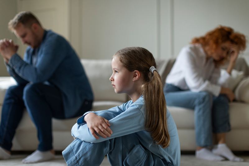 Child sitting between two distressed parents turned away from each other
