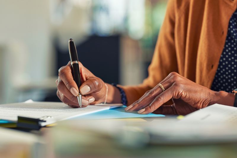 Person writing on paper with a pen at a desk